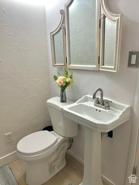 Half bathroom with toilet, wood finished floors, a textured wall, and baseboards