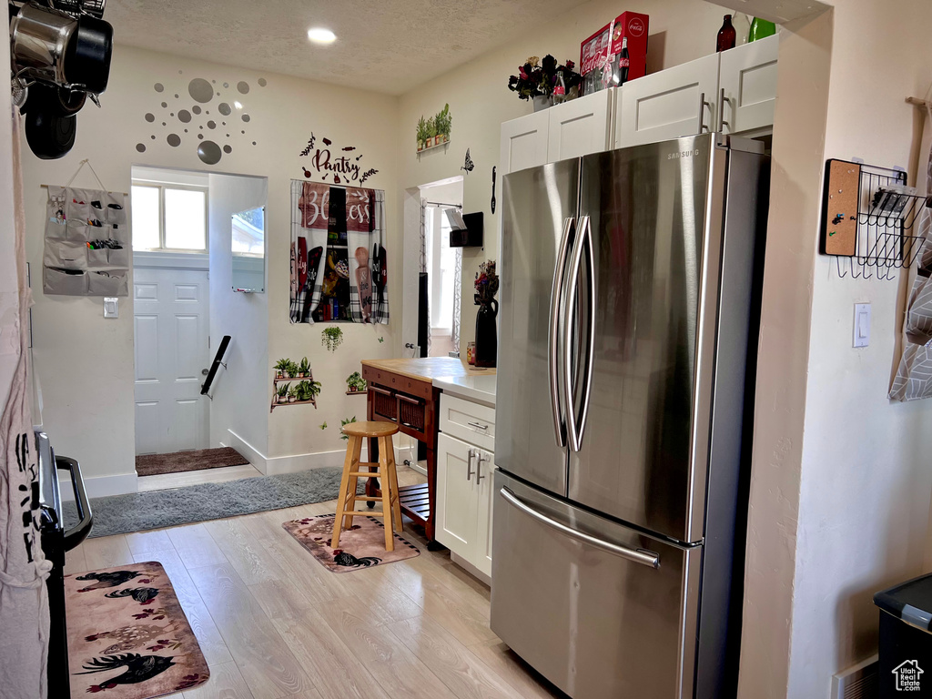 Kitchen featuring light wood-style floors, freestanding refrigerator, a textured ceiling, white cabinets, and light countertops