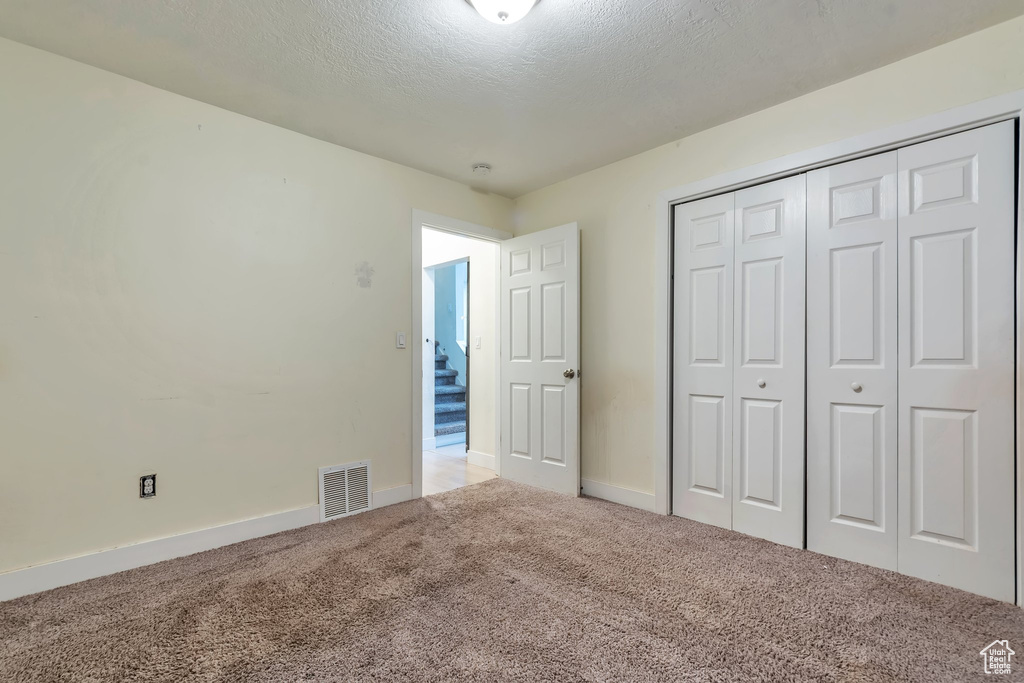Unfurnished bedroom with a textured ceiling, carpet flooring, and a closet