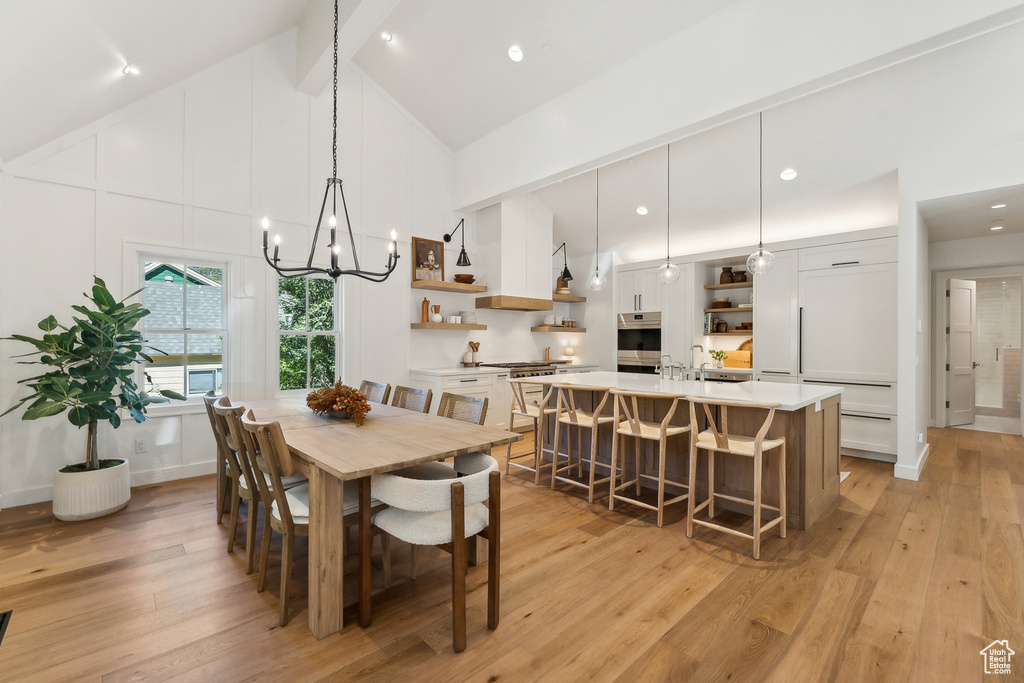 Dining room featuring beamed ceiling, high vaulted ceiling, an inviting chandelier, and light hardwood / wood-style floors