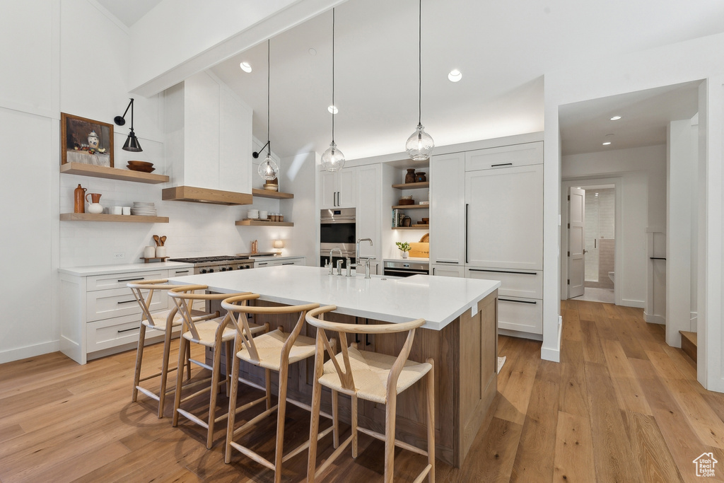 Kitchen featuring white cabinets, custom exhaust hood, pendant lighting, and light hardwood / wood-style floors