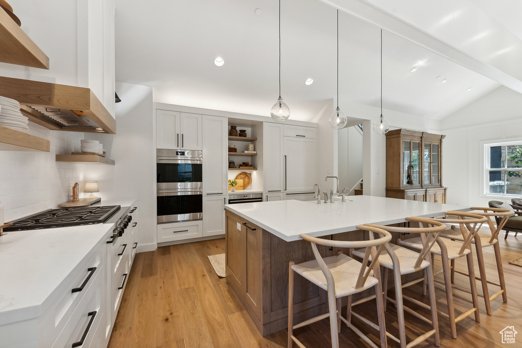 Kitchen featuring hanging light fixtures, lofted ceiling with beams, white cabinetry, and stainless steel appliances