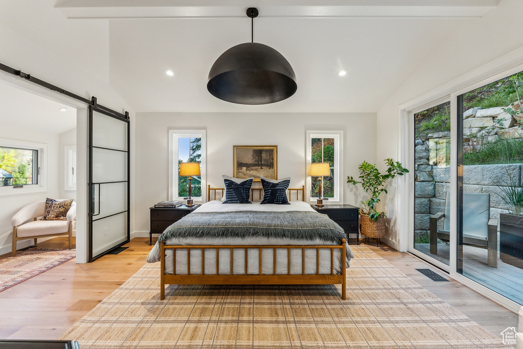 Bedroom with lofted ceiling, a barn door, light hardwood / wood-style flooring, and access to outside