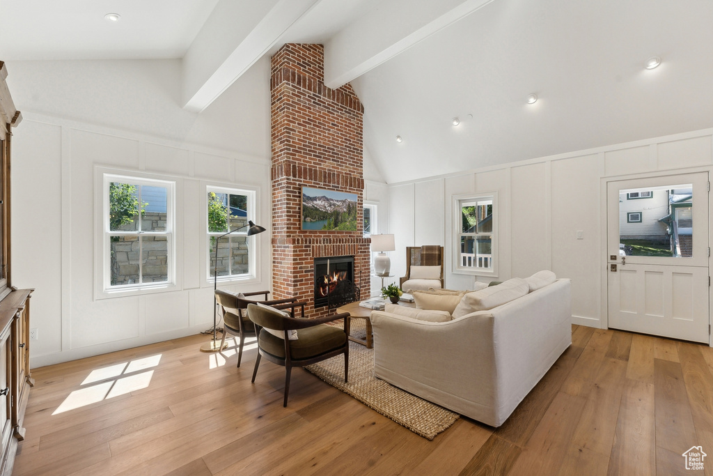 Living room featuring a fireplace, high vaulted ceiling, beam ceiling, and light hardwood / wood-style flooring