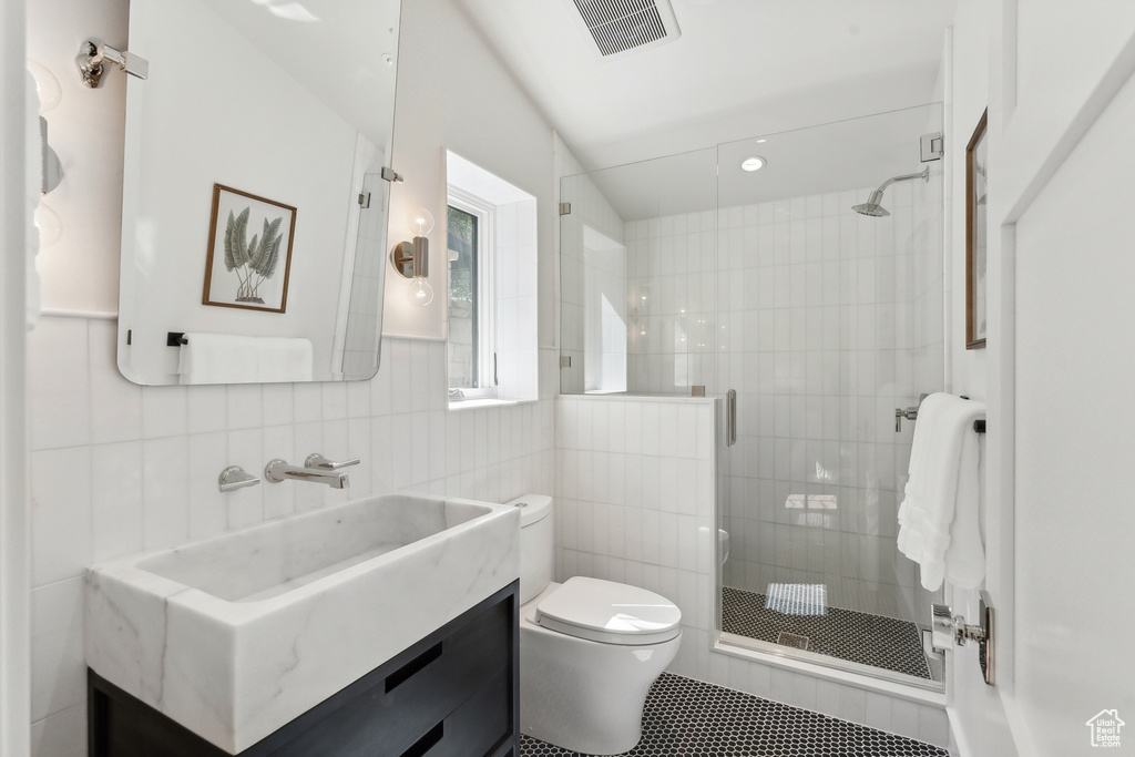 Bathroom with tile patterned flooring, walk in shower, toilet, tile walls, and vanity