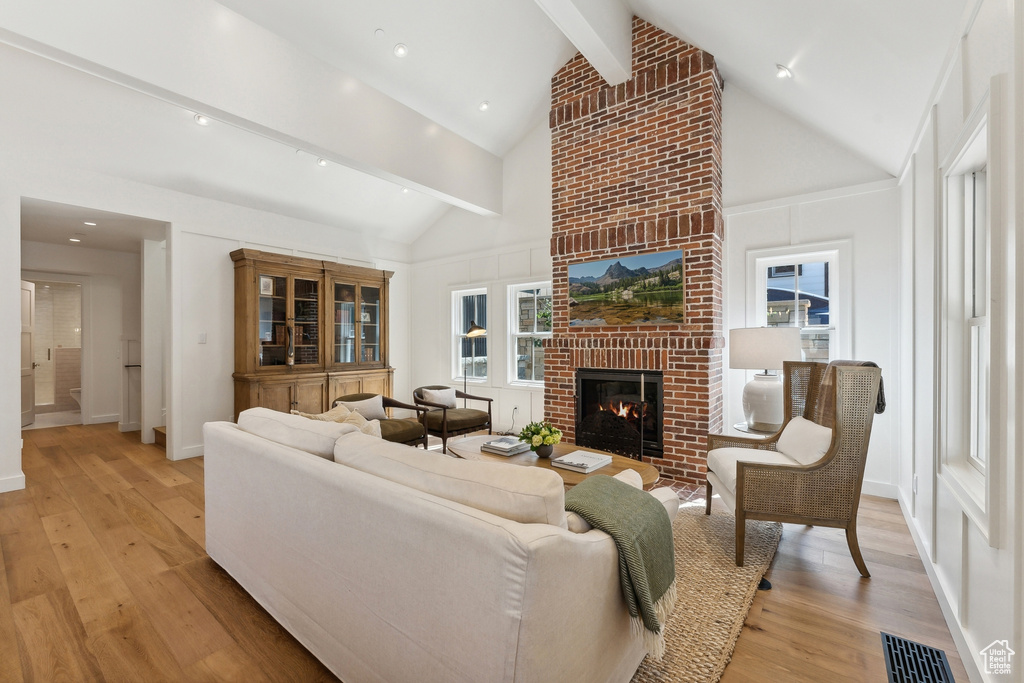 Living room with a brick fireplace, beamed ceiling, light hardwood / wood-style floors, and high vaulted ceiling