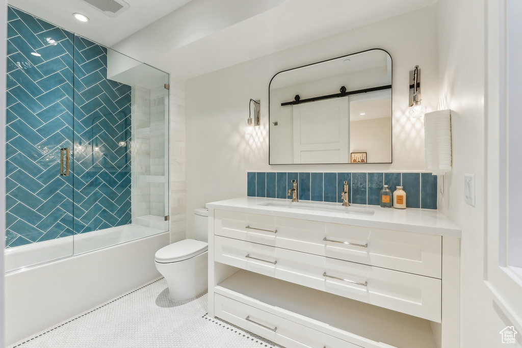 Full bathroom with vanity, tasteful backsplash, tile patterned floors, toilet, and shower / bath combination with glass door