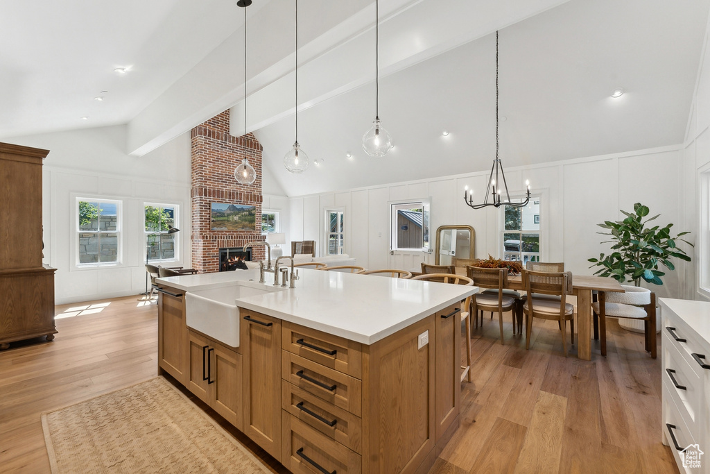 Kitchen featuring an island with sink, light wood-type flooring, sink, decorative light fixtures, and a fireplace