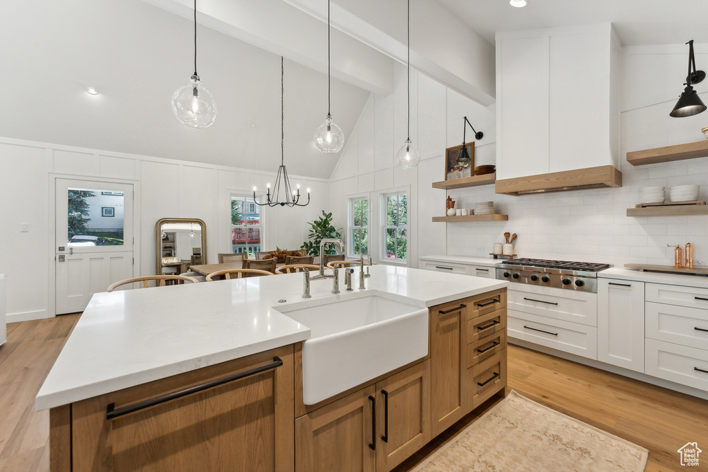 Kitchen with an island with sink, white cabinets, sink, light hardwood / wood-style floors, and decorative light fixtures