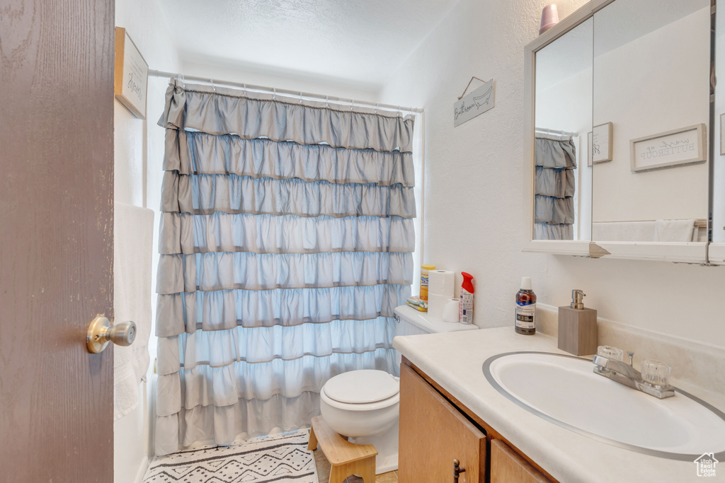 Bathroom featuring curtained shower, toilet, and vanity