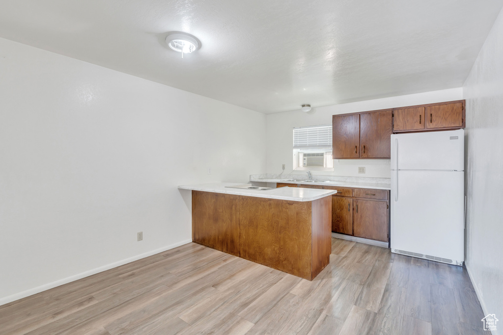 Kitchen with light wood-type flooring, white fridge, and kitchen peninsula