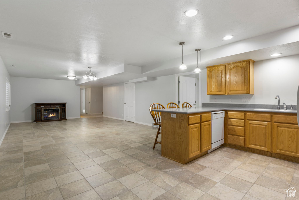 Kitchen with hanging light fixtures, white dishwasher, sink, kitchen peninsula, and a kitchen bar