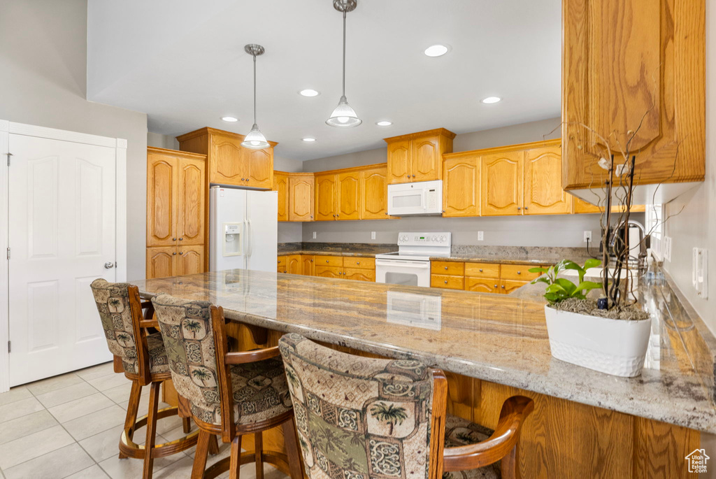 Kitchen with light tile patterned floors, white appliances, kitchen peninsula, a kitchen breakfast bar, and pendant lighting