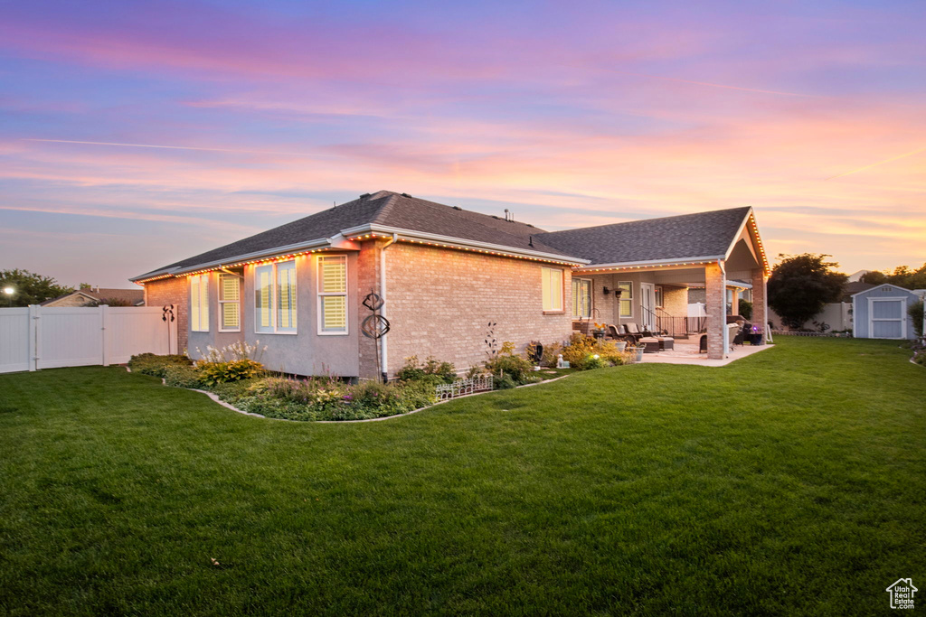 Back house at dusk with a yard, a patio area, and a shed