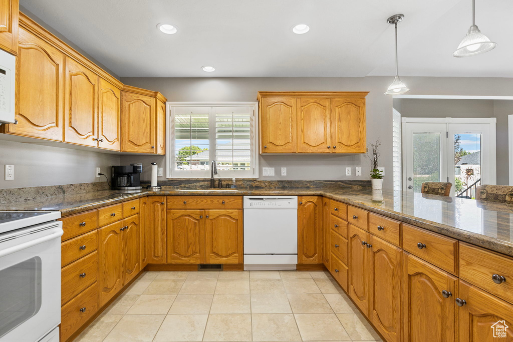 Kitchen with dark stone counters, pendant lighting, white appliances, sink, and light tile patterned flooring