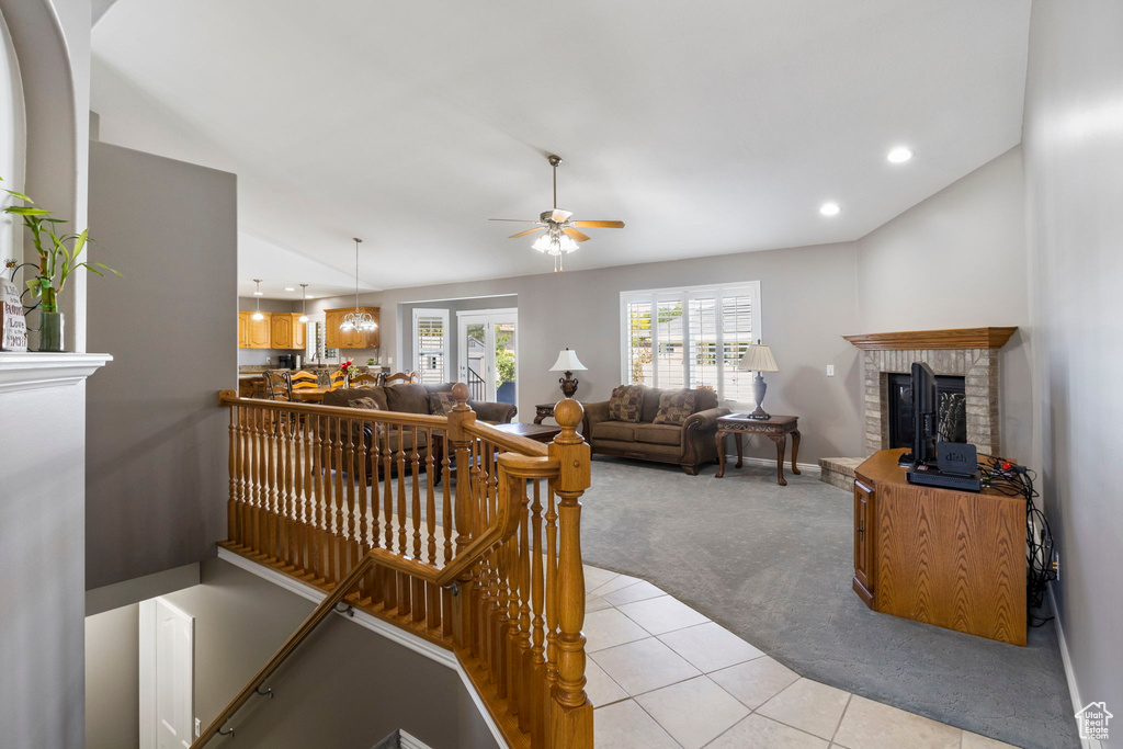 Carpeted living room with a fireplace, vaulted ceiling, and ceiling fan