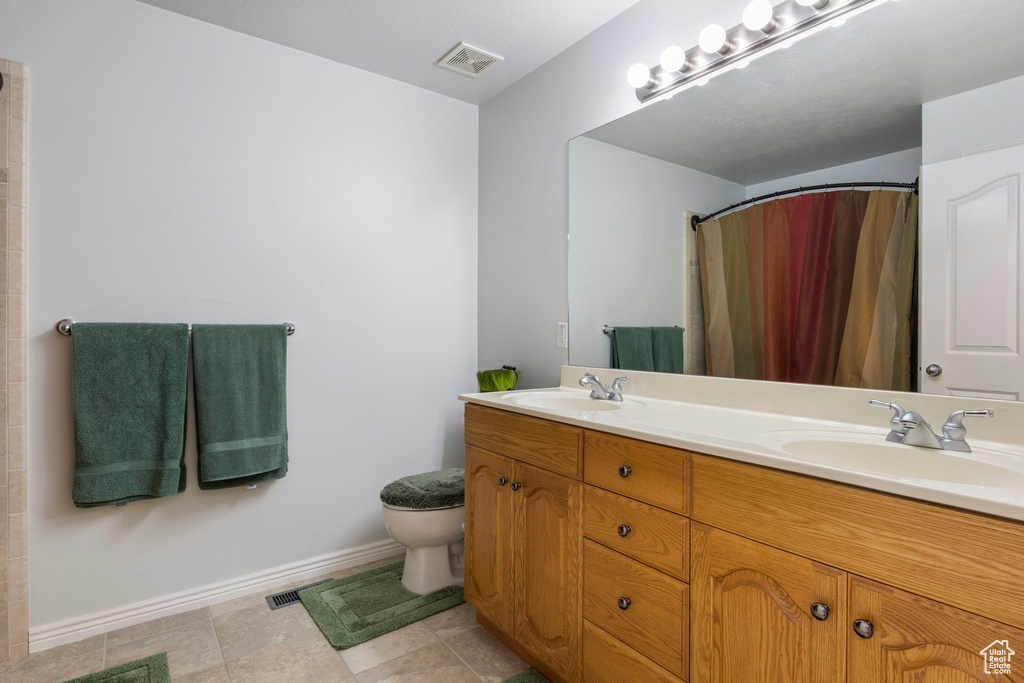 Bathroom with vanity, toilet, curtained shower, and tile patterned flooring