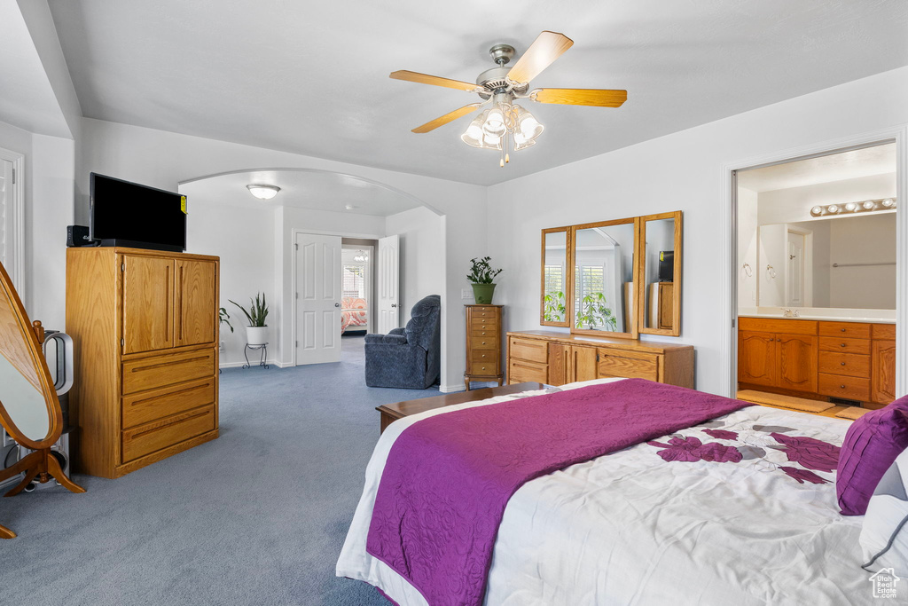 Carpeted bedroom featuring ceiling fan, ensuite bathroom, and multiple windows