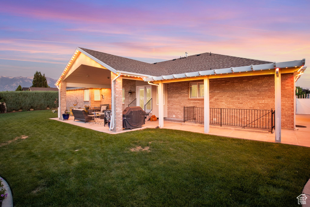 Back house at dusk with a patio area and a lawn