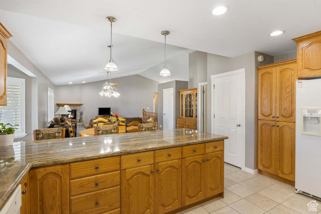 Kitchen with white refrigerator with ice dispenser, decorative light fixtures, light tile patterned floors, lofted ceiling, and stone counters