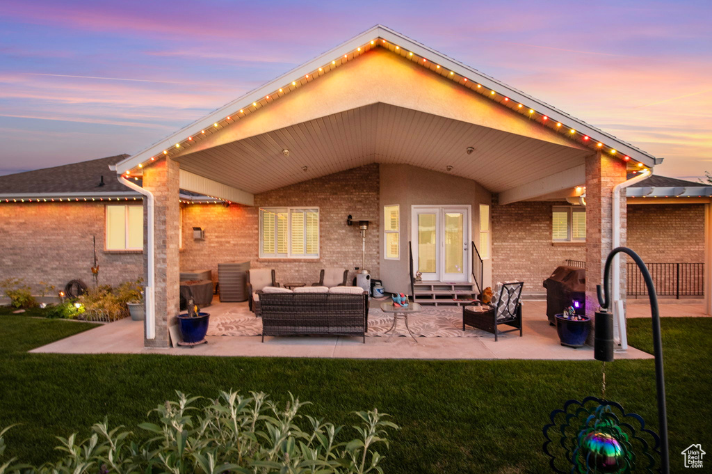 Back house at dusk featuring a yard, an outdoor living space, a patio area, and french doors