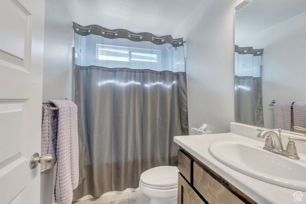 Bathroom with toilet, a shower with shower curtain, and vanity