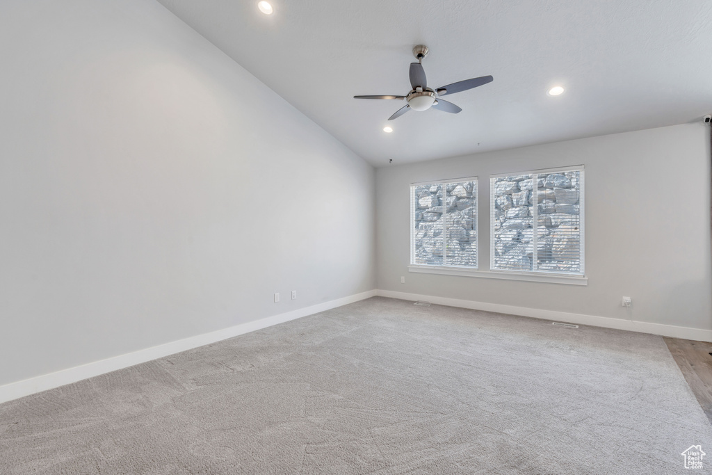 Carpeted empty room featuring ceiling fan and vaulted ceiling