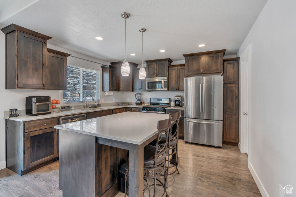 Kitchen featuring appliances with stainless steel finishes, sink, light wood-type flooring, a center island, and hanging light fixtures