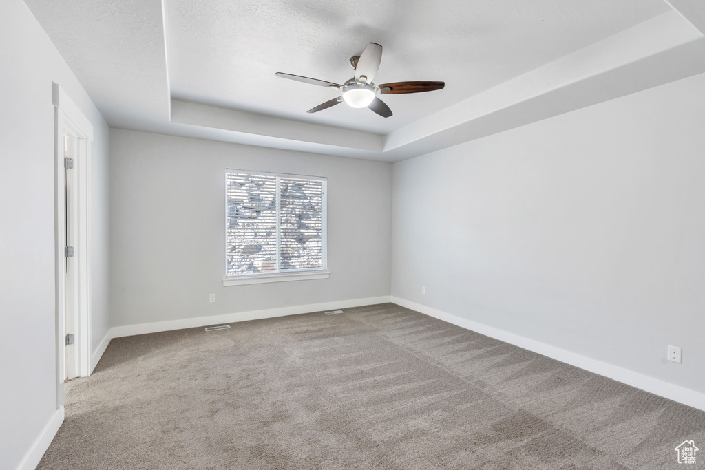 Spare room with ceiling fan, a raised ceiling, and light colored carpet