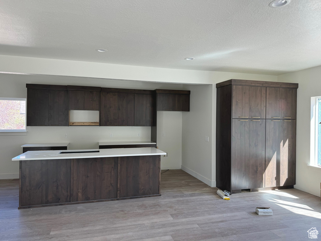 Kitchen with a center island, a textured ceiling, dark brown cabinetry, and light hardwood / wood-style floors