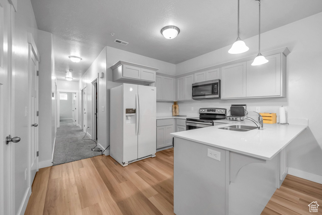 Kitchen featuring pendant lighting, appliances with stainless steel finishes, kitchen peninsula, sink, and light wood-type flooring