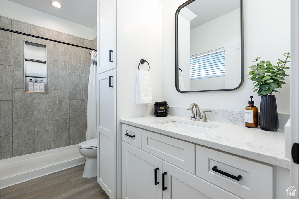 Bathroom featuring tiled shower, wood-type flooring, toilet, and vanity