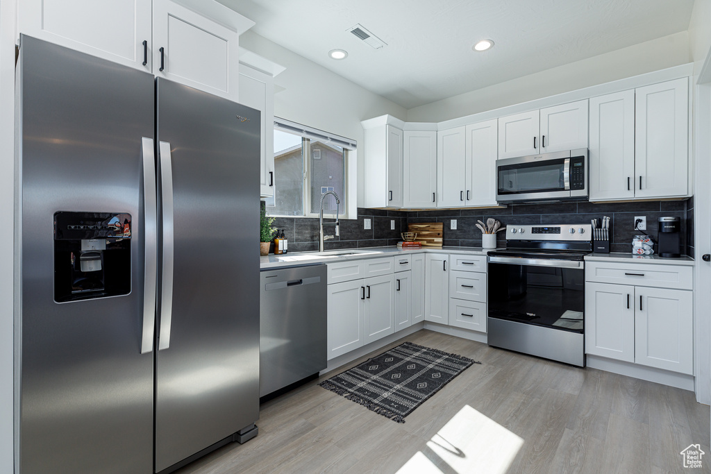 Kitchen with stainless steel appliances, decorative backsplash, white cabinetry, and light hardwood / wood-style flooring