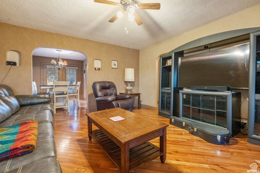 Living room featuring ceiling fan with notable chandelier, a textured ceiling, and hardwood / wood-style floors