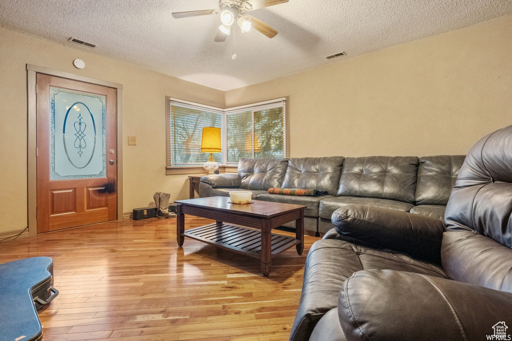 Living room with a textured ceiling, light hardwood / wood-style flooring, and ceiling fan