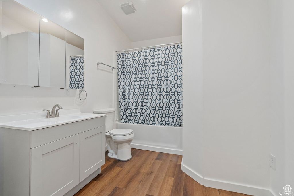 Full bathroom with vanity, toilet, hardwood / wood-style floors, and shower / bathtub combination with curtain