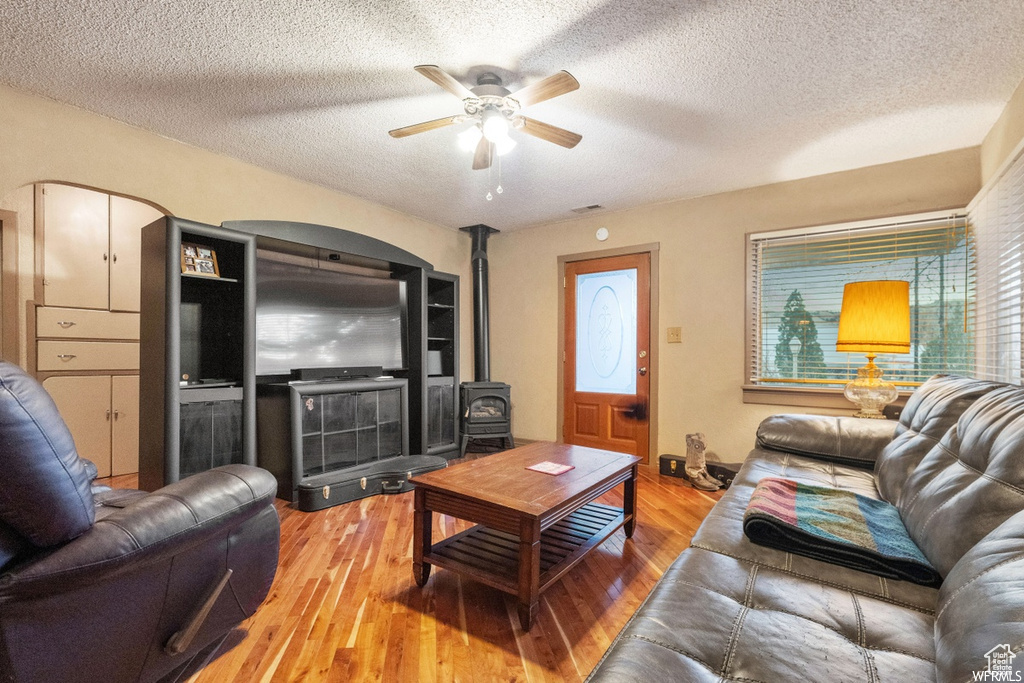 Living room with hardwood / wood-style floors, ceiling fan, a wood stove, and a textured ceiling