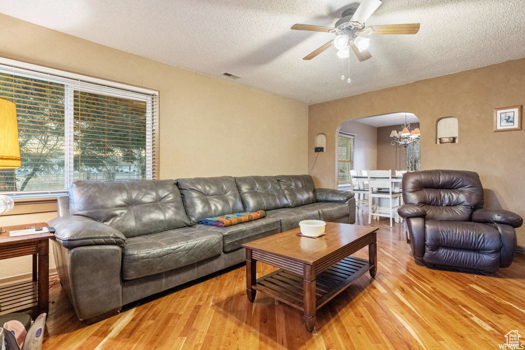 Living room with a healthy amount of sunlight, ceiling fan with notable chandelier, and light hardwood / wood-style floors