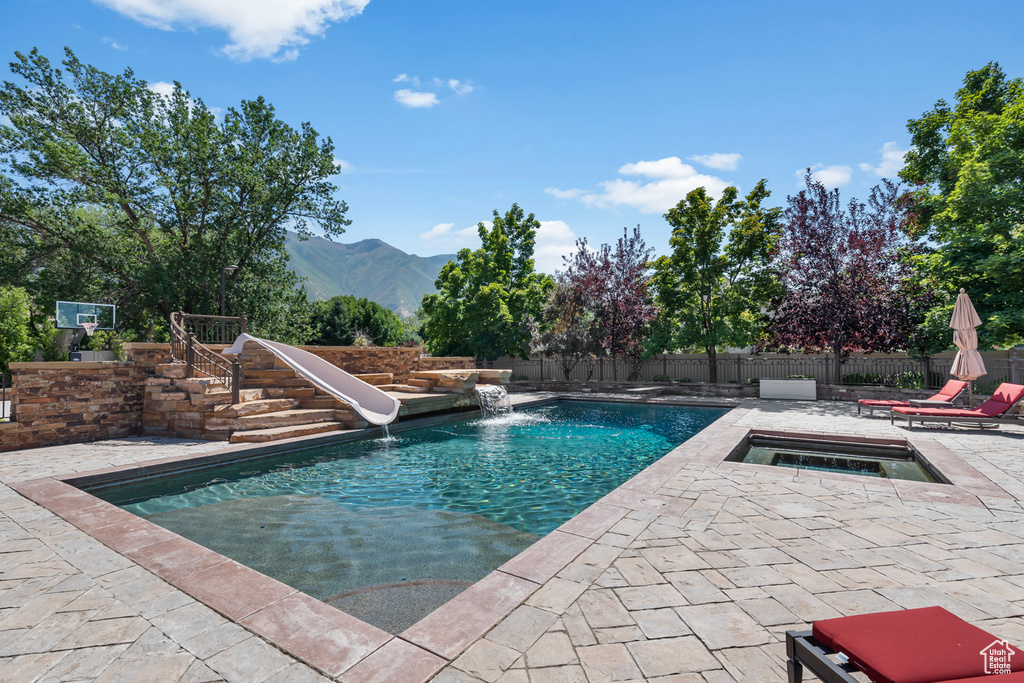 View of pool with pool water feature, a water slide, a patio area, and a mountain view