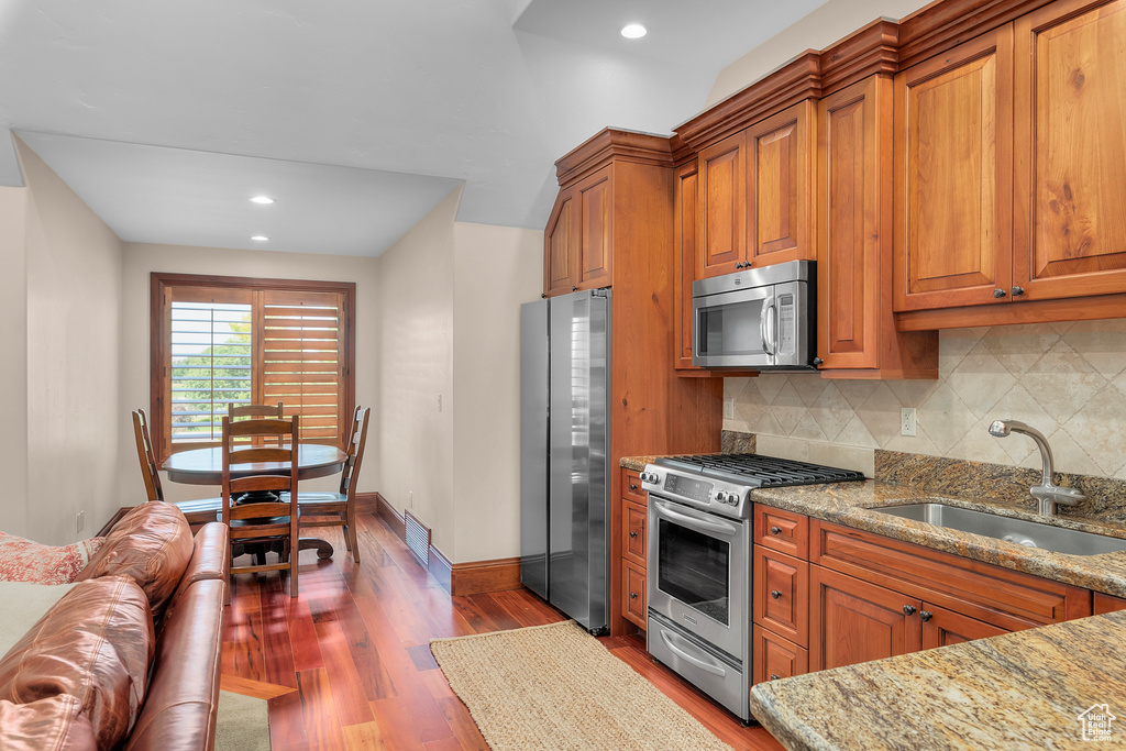 Kitchen with backsplash, dark hardwood / wood-style flooring, sink, light stone countertops, and appliances with stainless steel finishes