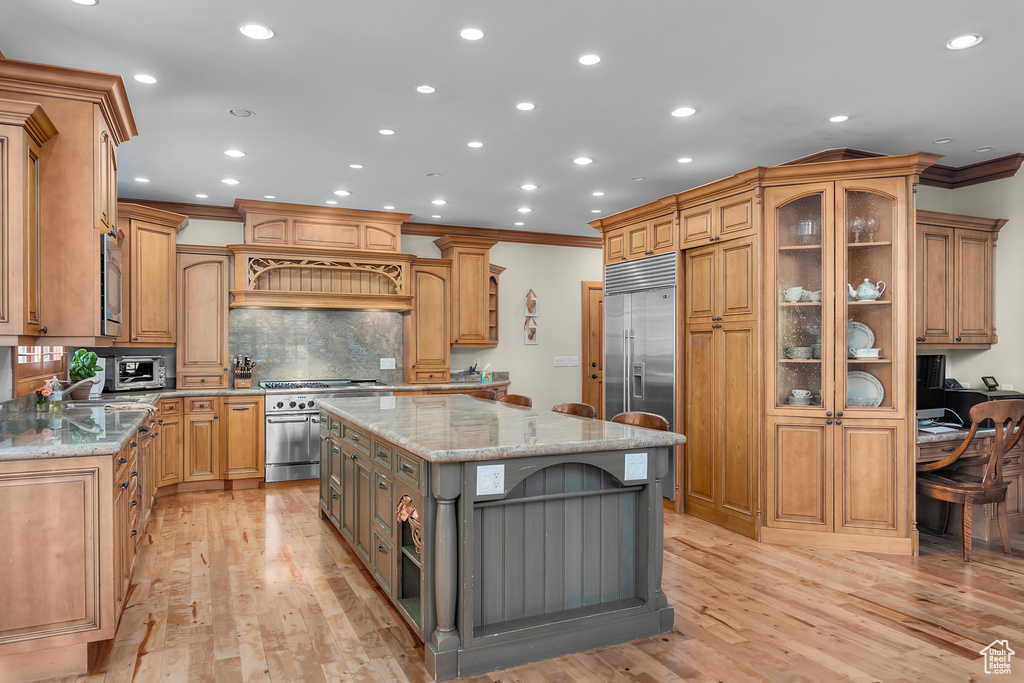 Kitchen featuring built in appliances, light hardwood / wood-style flooring, light stone counters, and a center island