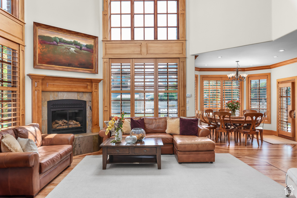 Living room featuring a tiled fireplace, ornamental molding, a chandelier, a towering ceiling, and hardwood / wood-style flooring