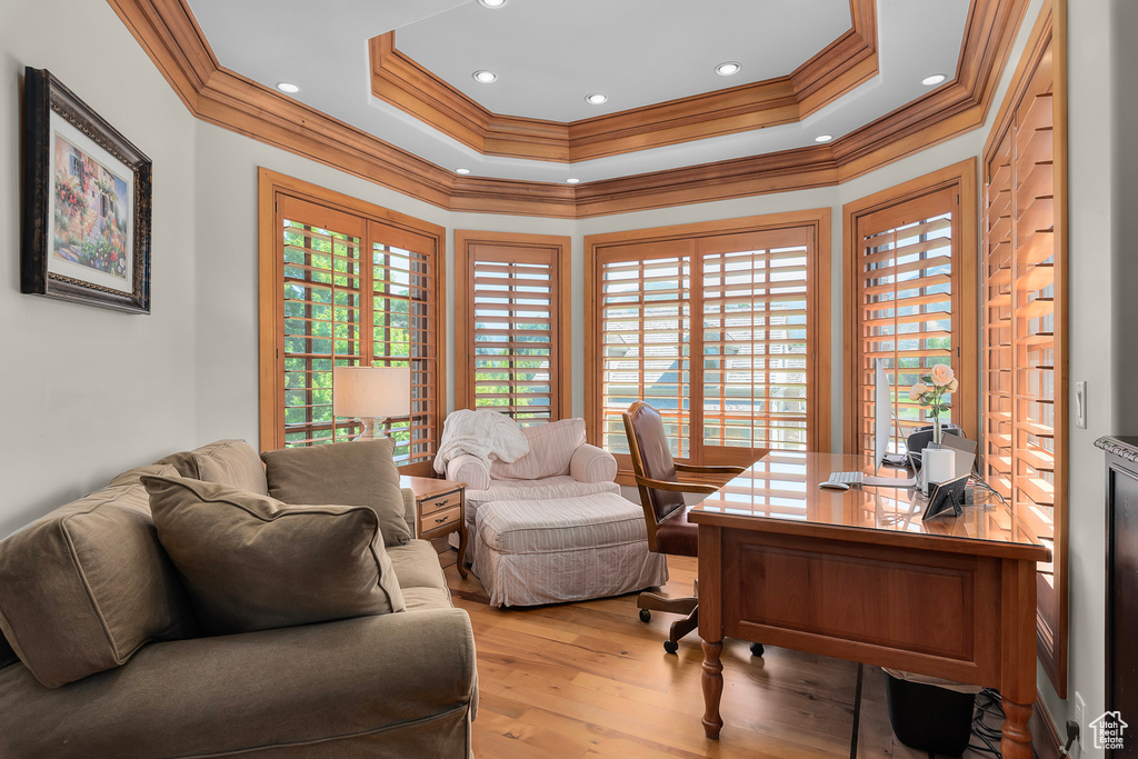 Office area with ornamental molding, light wood-type flooring, and a tray ceiling