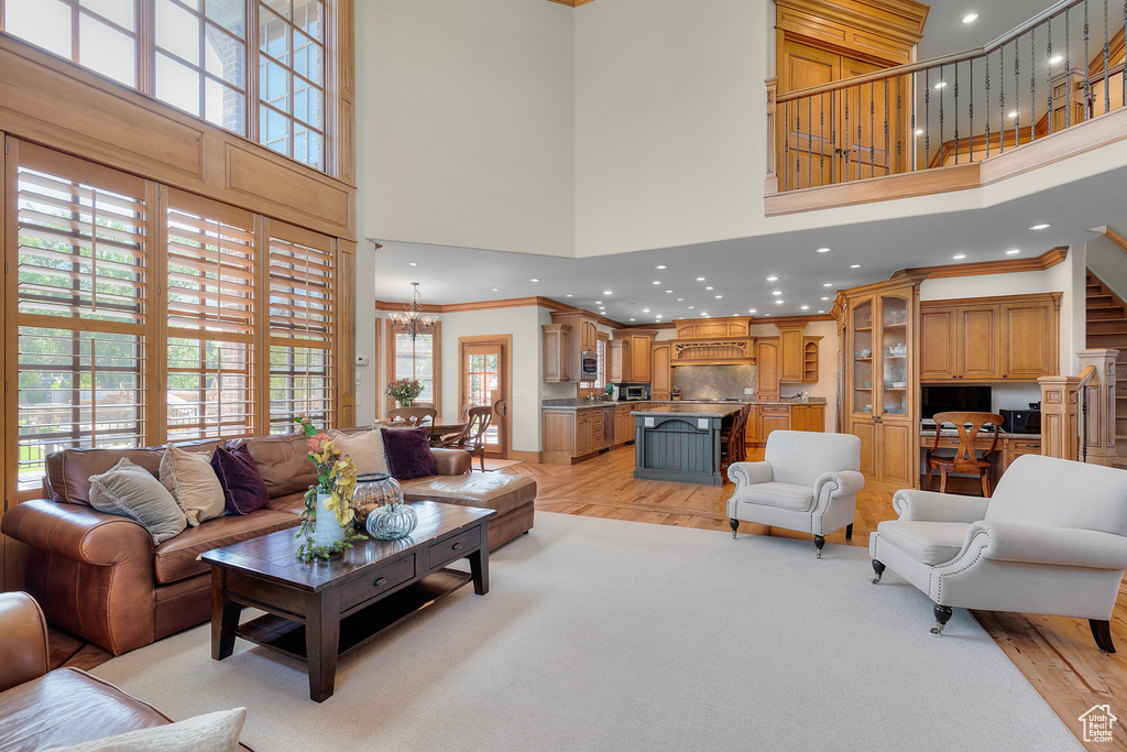 Living room featuring ornamental molding, light hardwood / wood-style flooring, a chandelier, and a high ceiling