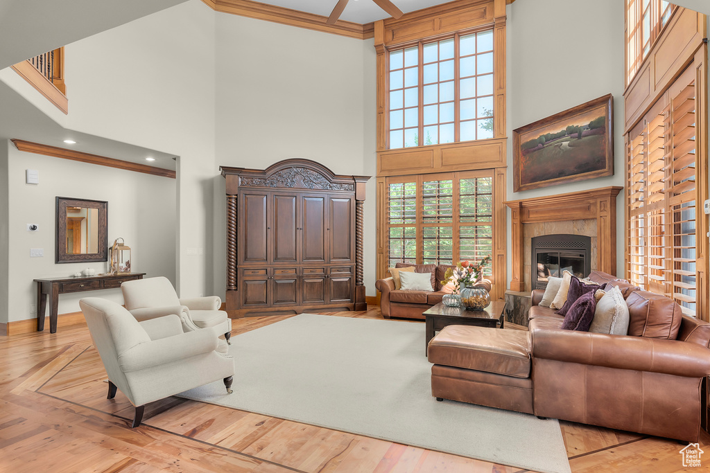 Living room with ornamental molding, ceiling fan, a towering ceiling, and light hardwood / wood-style floors