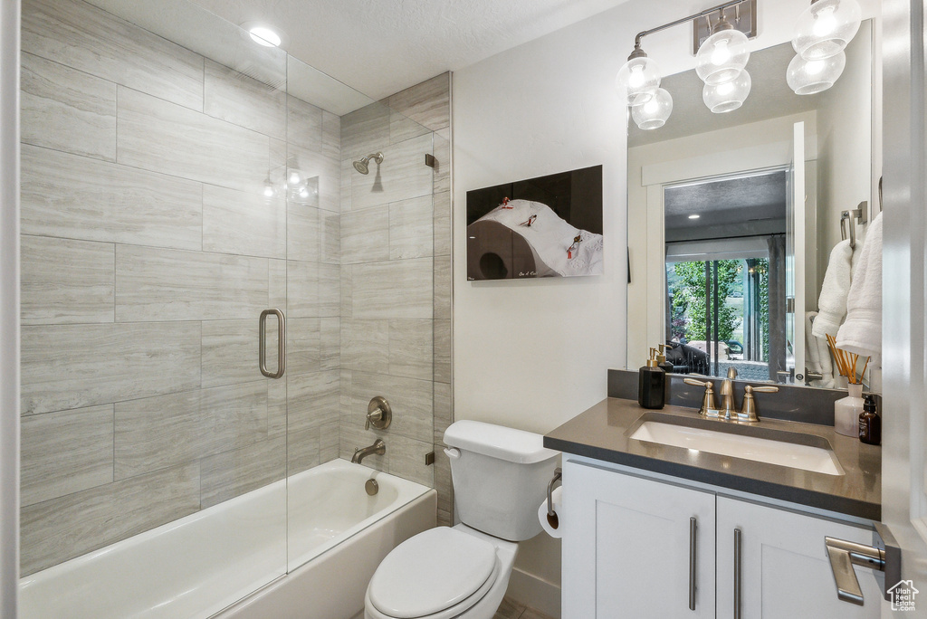 Full bathroom with shower / bath combination with glass door, vanity, toilet, and a textured ceiling