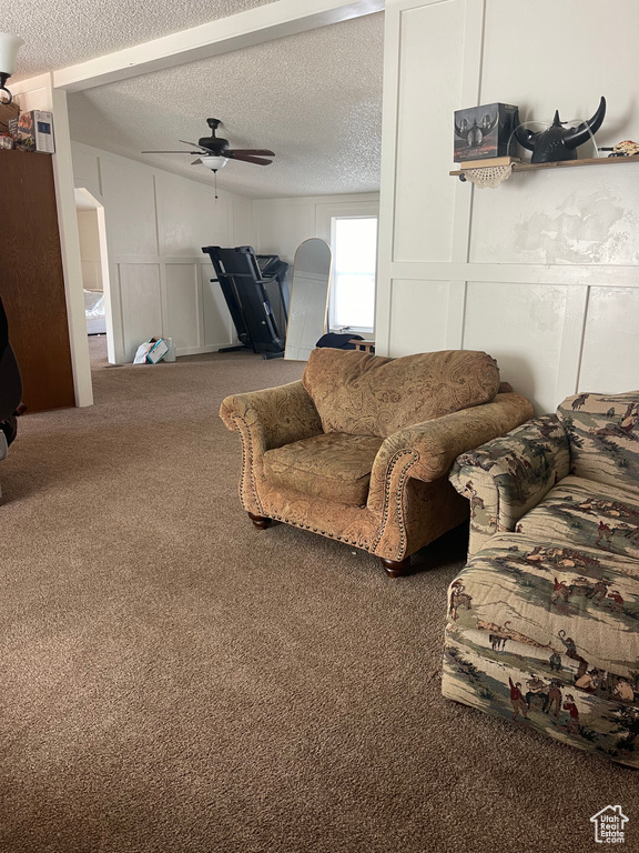 Carpeted living room featuring ceiling fan and a textured ceiling