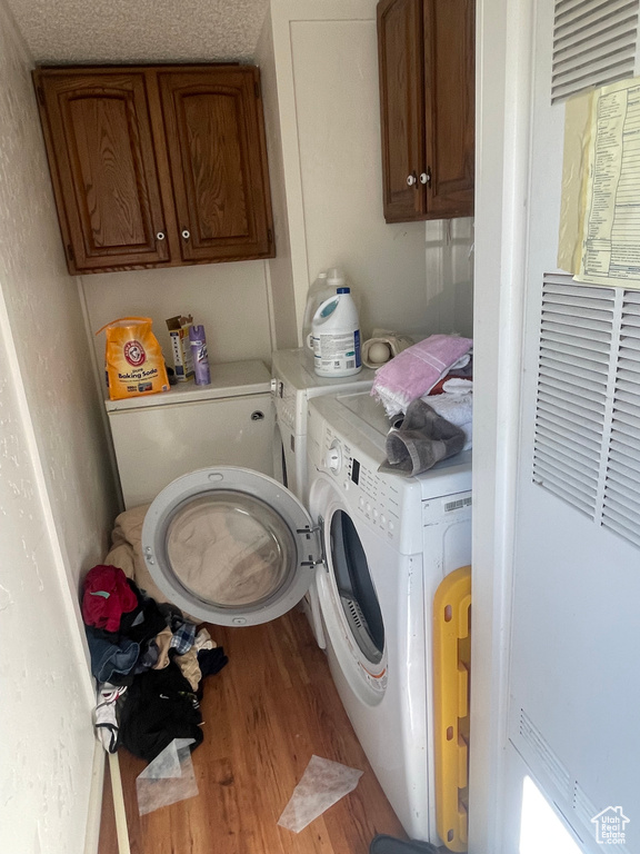 Laundry room featuring hardwood / wood-style floors, a textured ceiling, cabinets, and washer and dryer