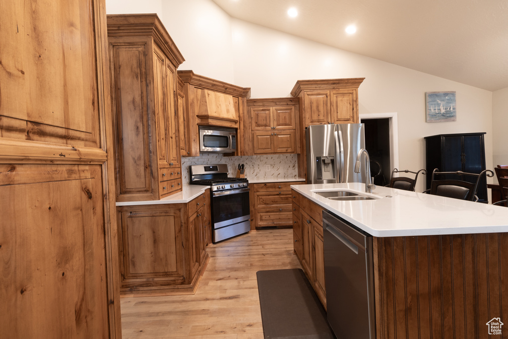 Kitchen featuring light wood-type flooring, a kitchen bar, stainless steel appliances, an island with sink, and sink