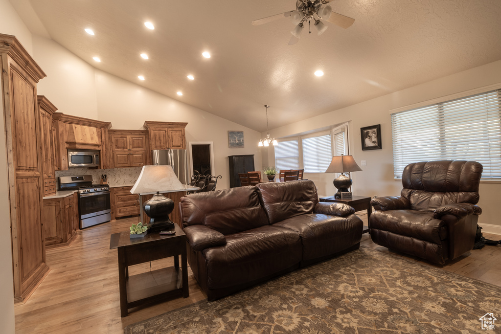 Living room featuring ceiling fan with notable chandelier, high vaulted ceiling, and hardwood / wood-style flooring